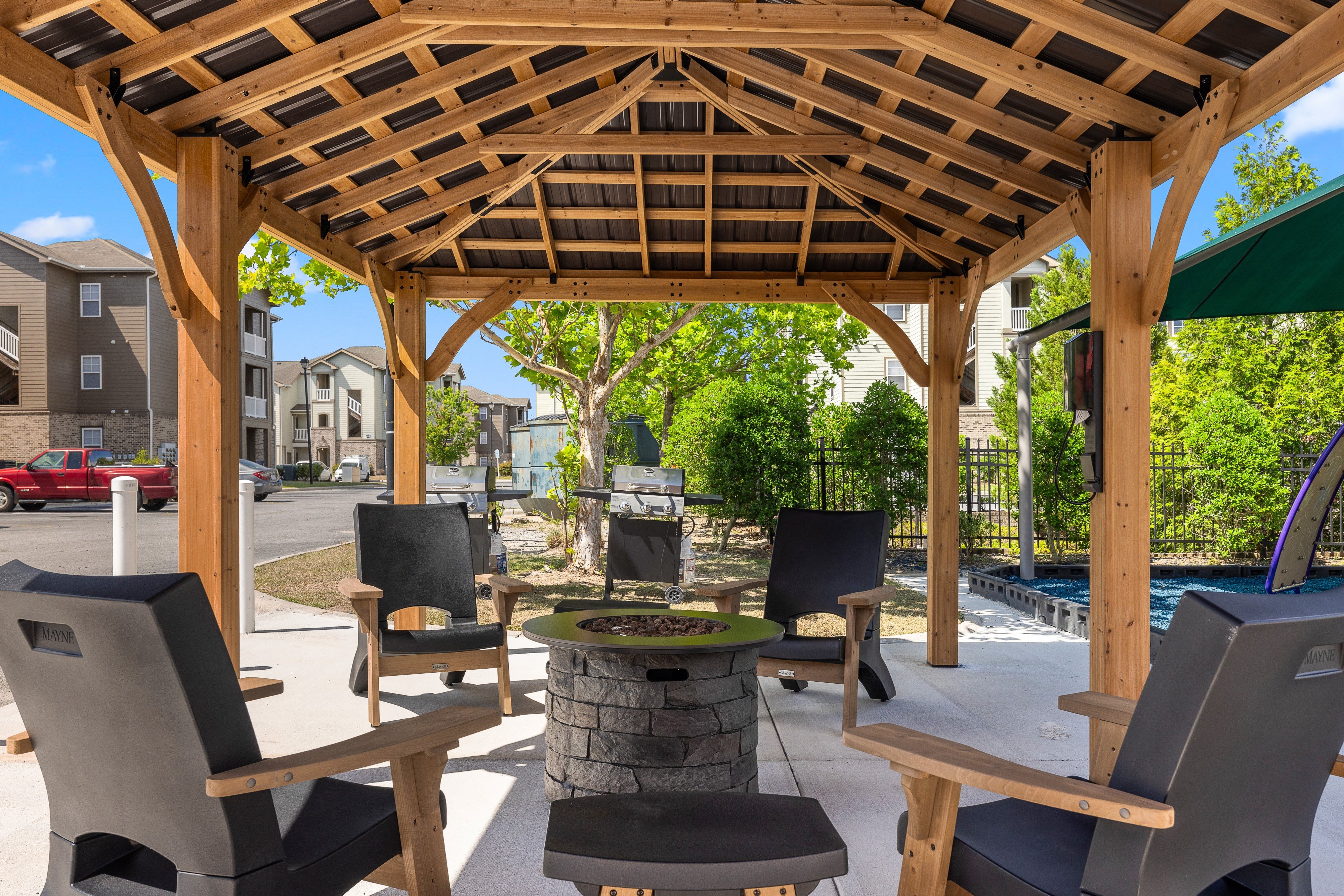 a patio with a fire pit and chairs under a wooden pavilion